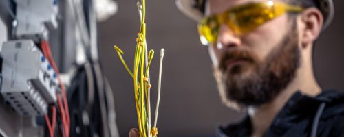 Male electrician at the checkout counter on a blurred background of a switchboard.